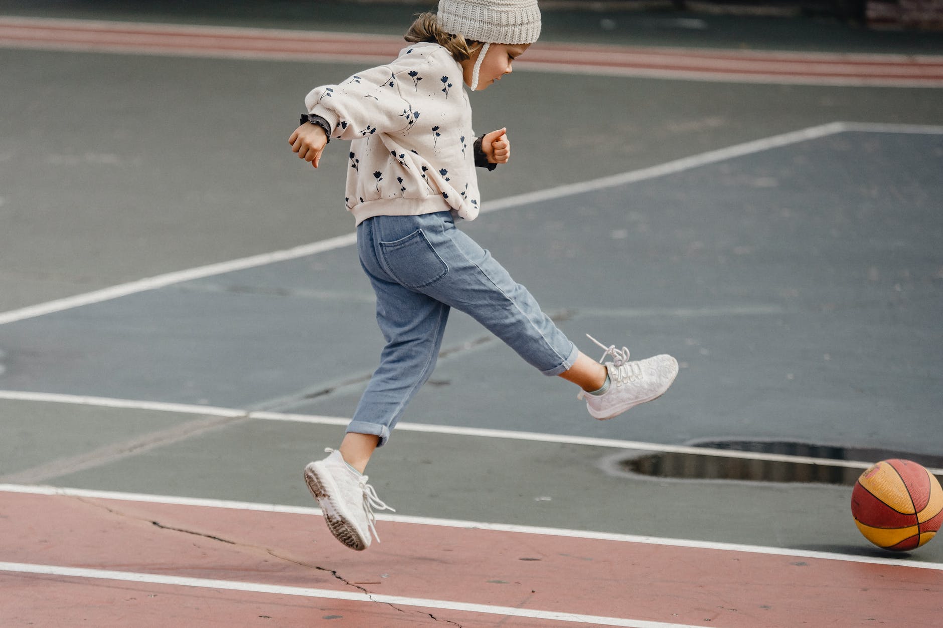 little girl jumping while playing with ball on sports ground